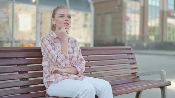 Pensive Young Woman Thinking While Sitting Outdoor on Bench