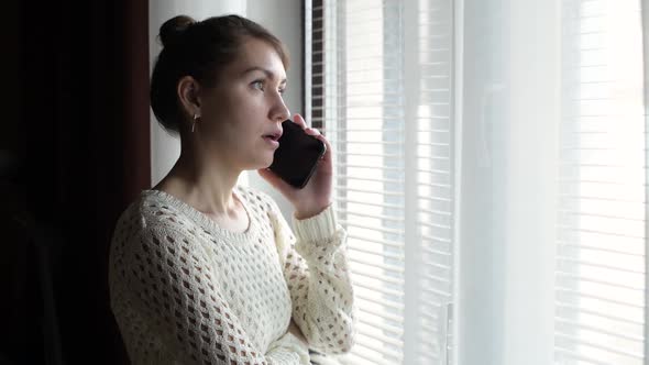 Girl standing near the window and talking on the phone