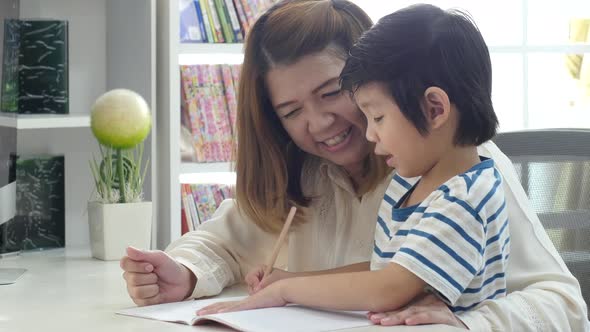 Asian Mother Helping Her Son Doing Homework On White Table