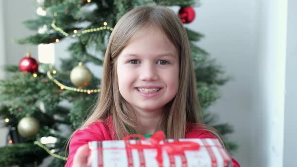Cute Little Girl Wearing Pajamas Holding Gift Box at Home Near Christmas Tree