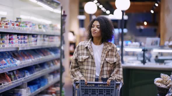Smiling African American Woman Walks Through Supermarket with Cart