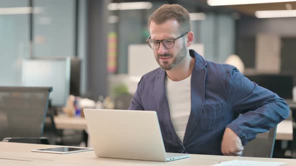 Middle Aged Businessman Having Back Pain While Using Laptop in Office