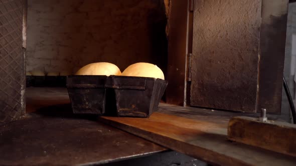 Baker places bread dough in oven with shovel.