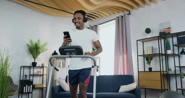 Black-Skinned Guy in Sportswear which Training on Treadmill at Home and Listening Modern Music