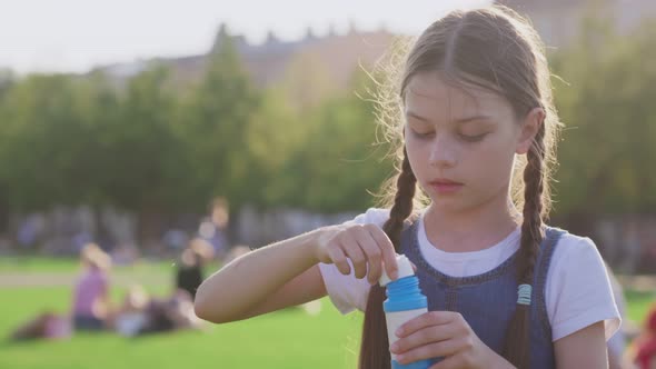 Medium Shot of Preteen Girl Blowing Soap Bubbles in Summer Park