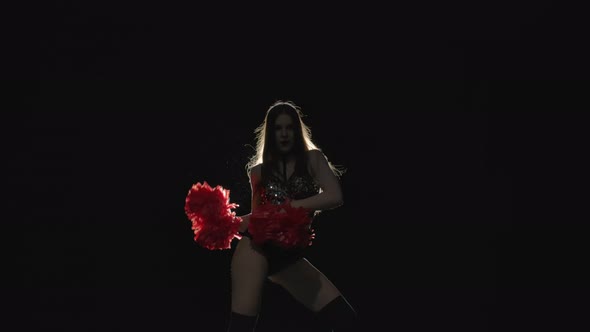 Energetic Dance of Cheering Performed By a Cute Cheerleader Holding Pompoms Against Backlit Black