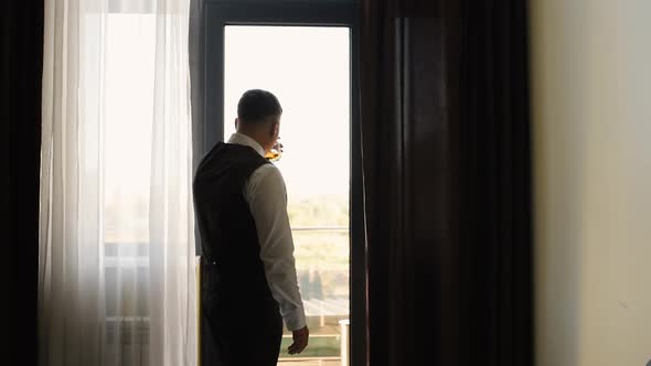 Man Groom Businessman Successful Stands in Apartment Panoramic Window Holding Glass Whiskey