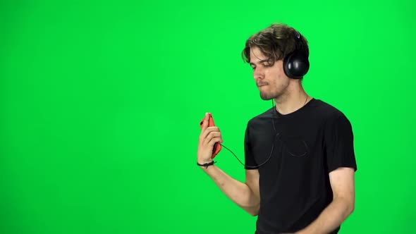 Man in Big Headphones Goes and Dances with Smartphone on Green Screen at Studio. Slow Motion