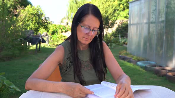 middle-aged woman reading a book in the backyard of her home