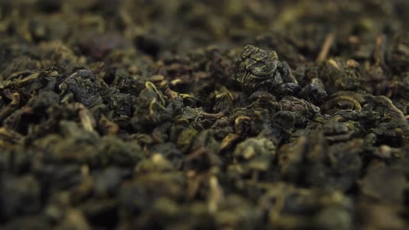 Dried rolled green tea leaves fall in slow motion into a heap