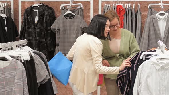 Young Woman Chooses a Dress in a Clothing Store and Consults with Her Friend