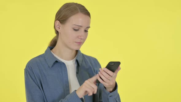 Young Woman Browsing Smartphone on Yellow Background