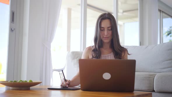 Beautiful Woman Freelancer Working with Laptop and Graphic Tablet in Lit Room