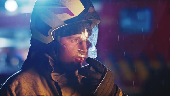 Portrait Shot of a Fireman Speaking on the Walkie Talkie and the Site During the Rain. Fire