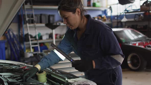 Female mechanic using a led lamp and repairing a car at a car service station