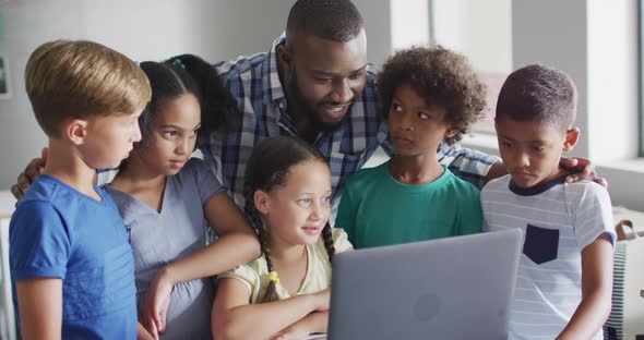 Video of happy african american male teacher and class of diverse pupils working on laptop