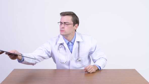 Young Handsome Man Doctor Making Decisions Against Wooden Table