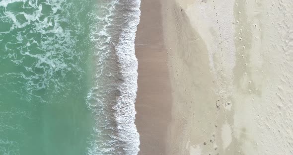 Static top down view of tropical beach, foamy ocean waves washing sand. Waves hitting sand beach