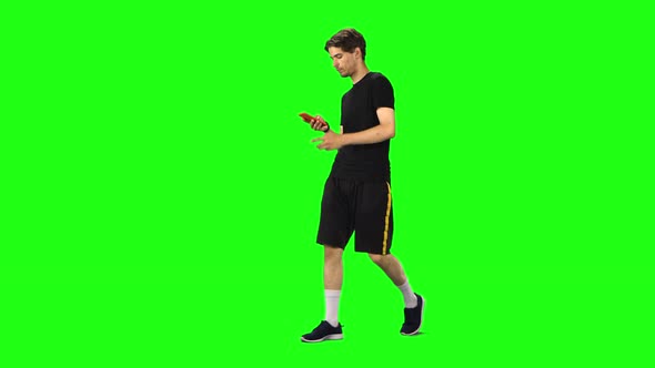 Brunette Man Goes and Texting with Smartphone on Green Screen at Studio.