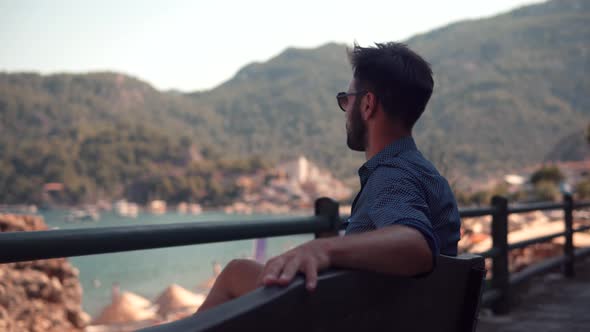 Guy In Sunglasses Sitting On Bench And Thinking. Romantic Man Rest And Looks At Ocean Italian Man.