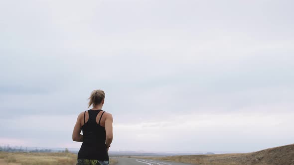 Woman of Athletic Build in Sportswear Jogging Outdoors Background Sky Back View