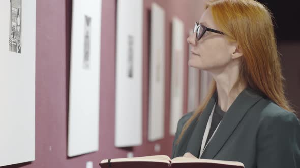 Female Journalist Looking at Artwork in Gallery and Taking Notes