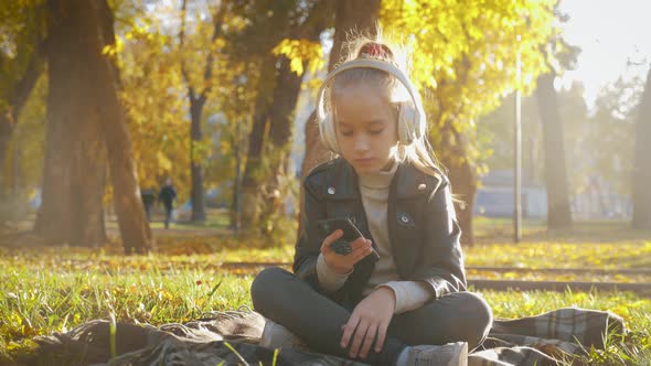 Young Girl in Headphones Listening To Music and Sings Favorite Songs in the Autumn City Park. The