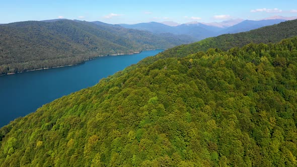 Aerial view over mountain lake with turquoise water and green trees forest