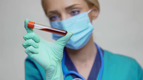 Medical Doctor Nurse Woman Wearing Protective Mask and Latex Gloves - Holding Blood Test Tube