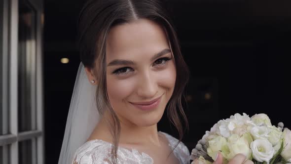 Bride in Wedding Dress and Veil with Bouquet of Flower From Groom Stay Near Balcony Doors at Home