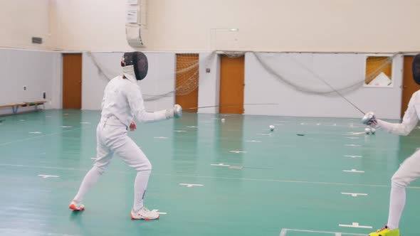 Two Young Women in Full Protection of White Suits Having an Active Fencing Training in the School