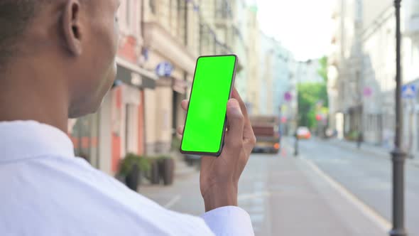 Rear View of African Man Looking at Smartphone with Green Chroma Screen