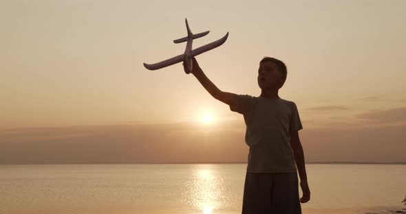 Happy Kid Playing with Toy Airplane Against Orange Sun Summer. Best Childhood Concept