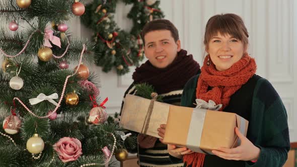 A Beautiful Young Couple in Love Near the New Year Tree Giving Presents to the Viewer