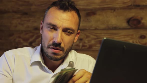 A Distressed Businessman Looks at the Camera Holds a Bundle of Dollars Losses