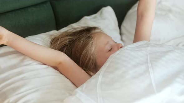 Cute little girl child wakes up in the morning in bed in the bedroom on an orthopedic mattress