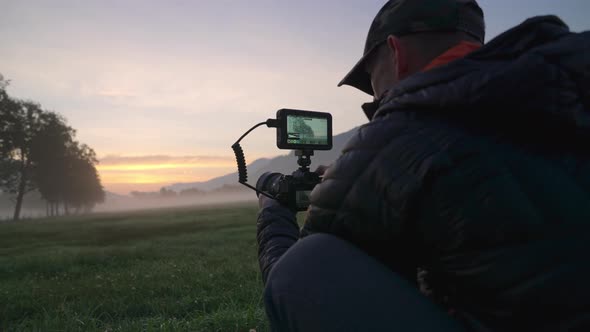 Man Adjusting Camera With Monitor In Dawn Landscape