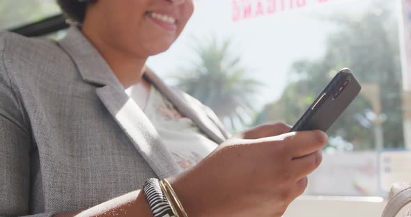 Happy plus size biracial woman using smartphone in bus