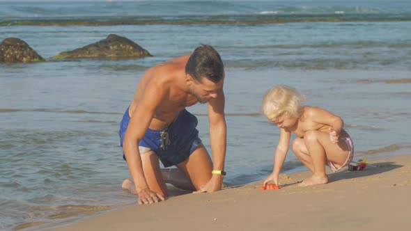 Man Plays with Little Daughter in Sand Spending Family Time