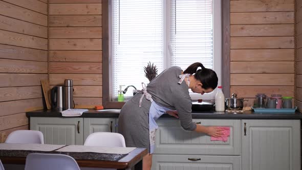 Young Woman Wiping Kitchen Cabinets at Home