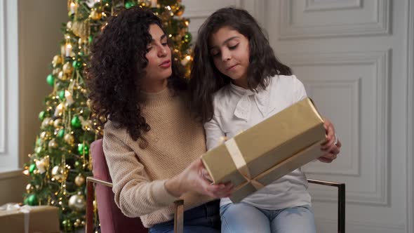 Little Daughter Opens a Christmas Gift with Her Mother