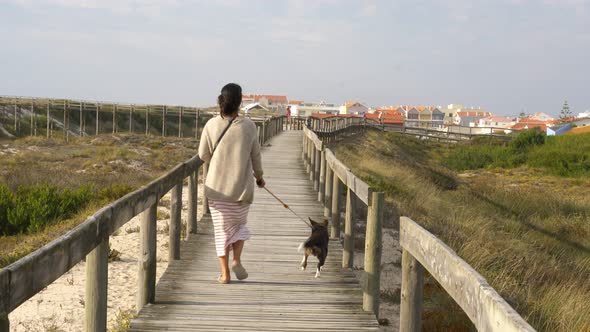 Caucasian woman walking with dog near a beach wooden path in Costa Nova Aveiro, Portugal