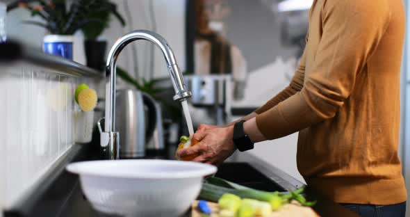 Man washing capsicum with water under the tap