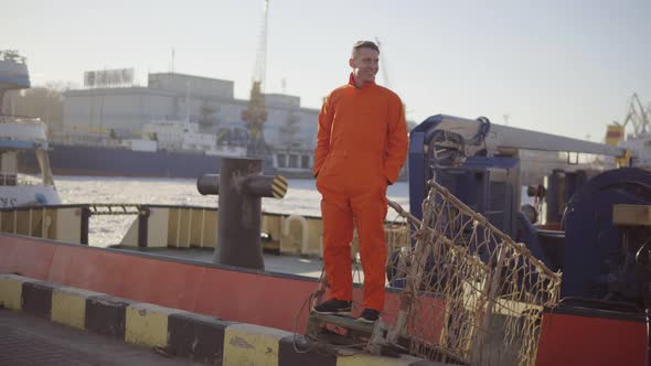 Young Worker in the Uniform Posing on the Bridge of a Ship About to Moor Off in a City Harbor