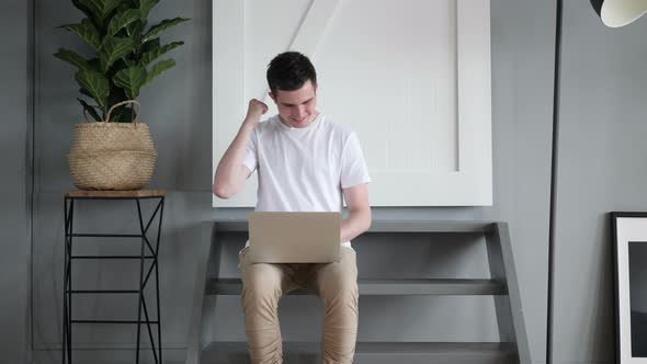 Excited Man Celebrating Win on Laptop while Sitting on stairs