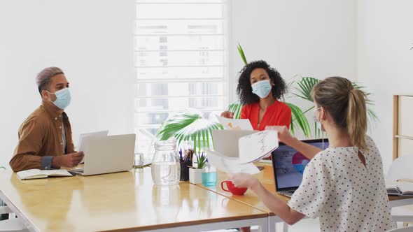 Woman wearing face mask showing a document to her colleague at office