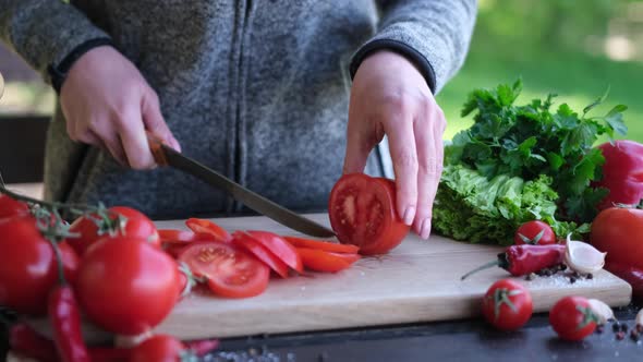 Female Slicing Tomato for a Picnic on Wooden Cutting Board Outddors