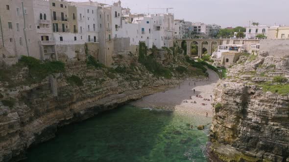 Slow aerial flyover of Lama Monachile beach in Polignano a Mare, Italy with sea and cliffs and waves