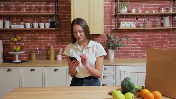 Woman Browsing on Mobile Phone at Home Kitchen. Young Woman Browsing on Smartphone Smiling Happy.