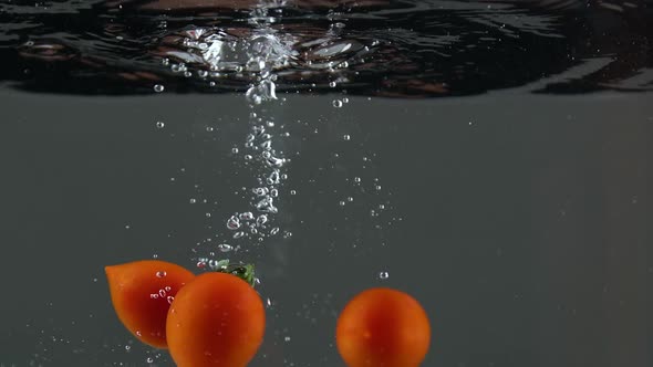 Closeup of Fresh and Health Cherry Tomatoes Falling Into Clear Water with Big Splash on Black